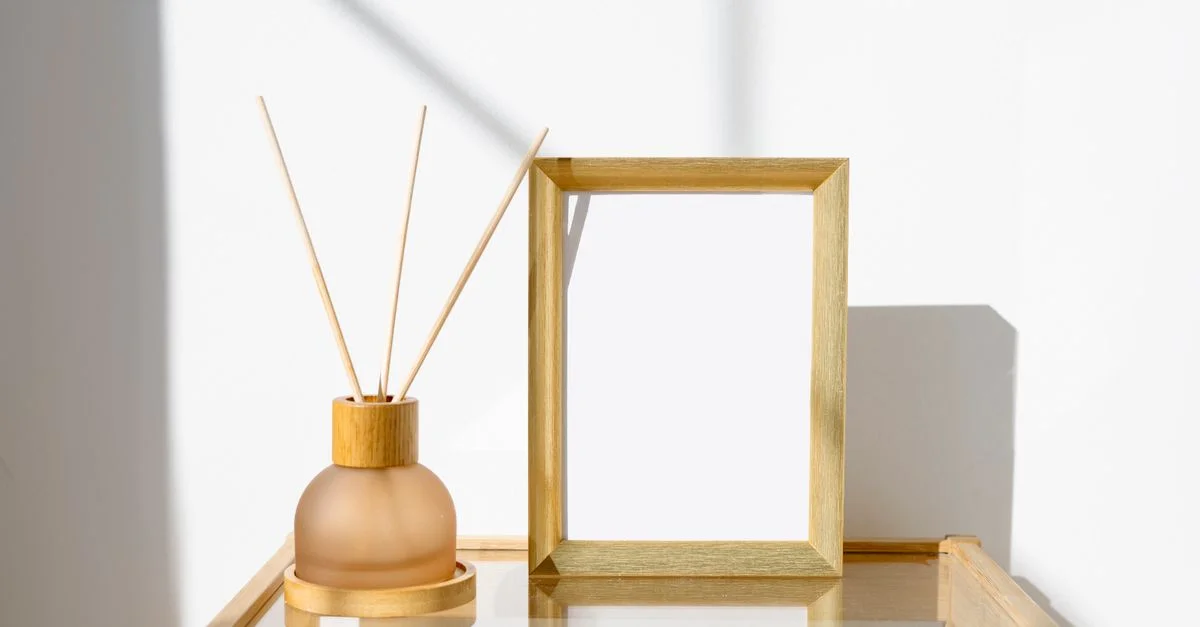 Configuración minimalista elegante con un marco de madera y un difusor de aroma sobre una mesa de cristal con luz natural.
