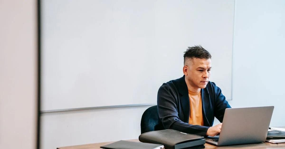 Hombre de negocios concentrado escribiendo en el portátil en el escritorio de la oficina con pizarra.