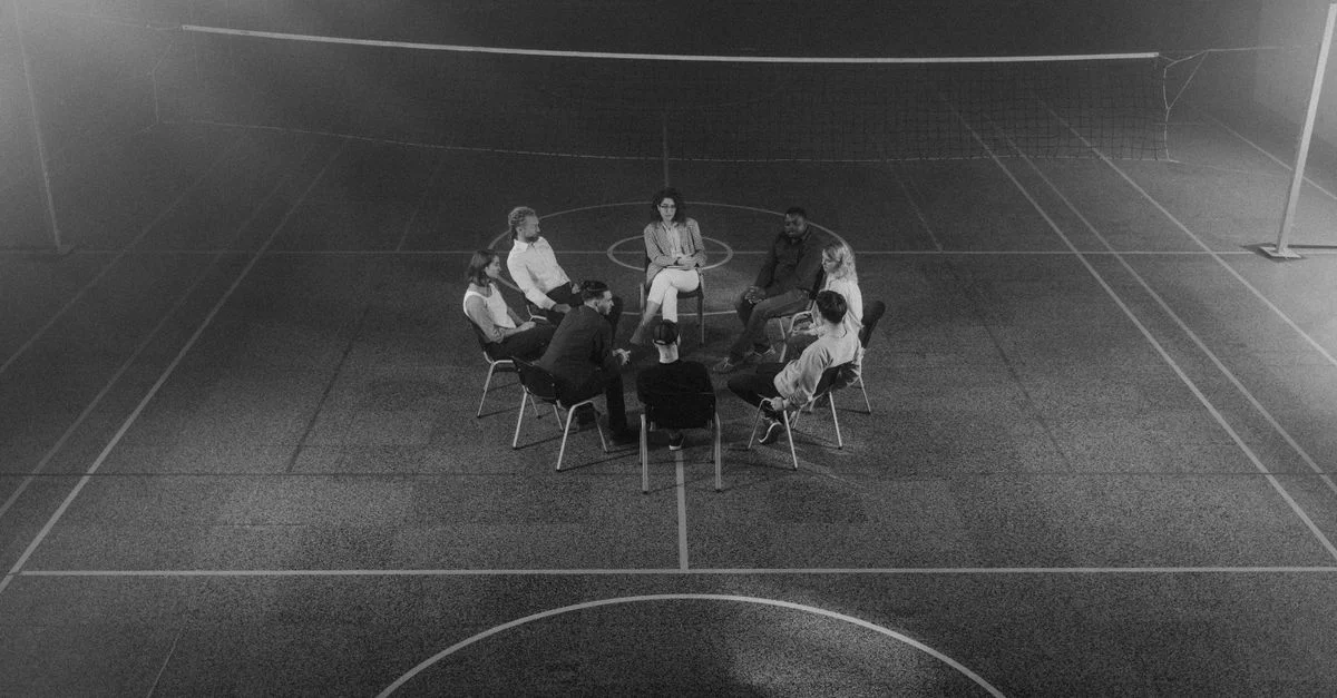 Un groupe de thérapie assis en cercle dans une salle de sport faiblement éclairée.