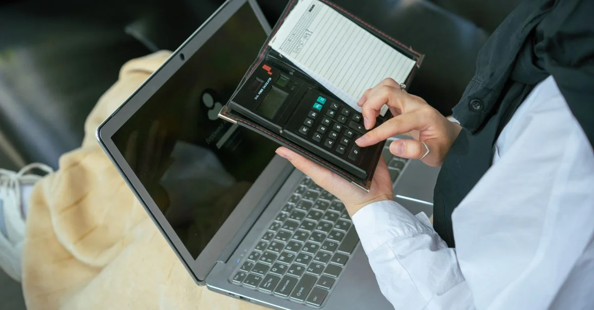Primer plano de una persona usando una calculadora con un portátil, simbolizando la productividad en el hogar.