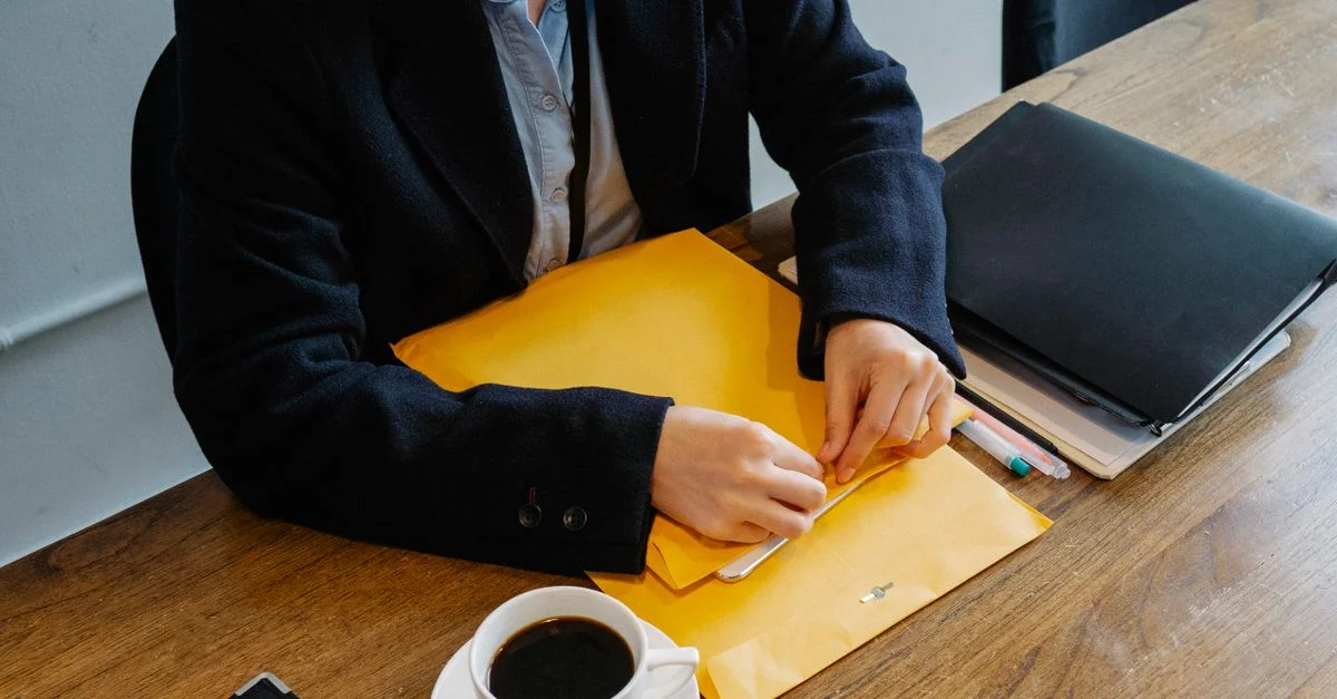 Una mujer de negocios con traje formal sosteniendo documentos con una taza de café sobre una mesa de madera.