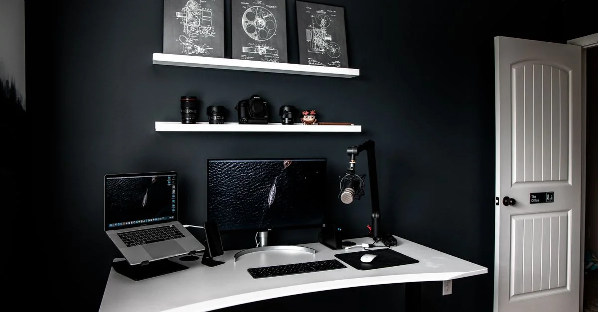Una configuración de oficina en casa elegante con monitores duales, un micrófono y decoración de tonos oscuros.