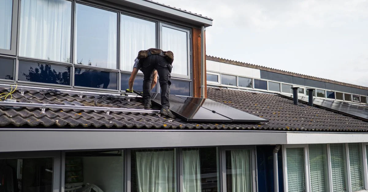 Técnico trabajando en la instalación de paneles solares en un tejado residencial durante el día.